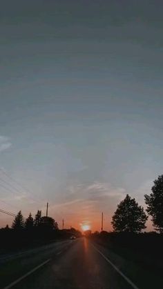 the sun is setting behind some trees on the side of the road with power lines in the distance