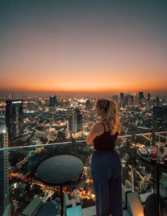 a woman standing on top of a tall building looking at the city lights in the distance