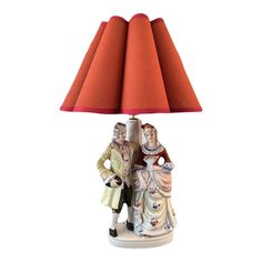 a table lamp with a red shade on it and two people standing next to each other