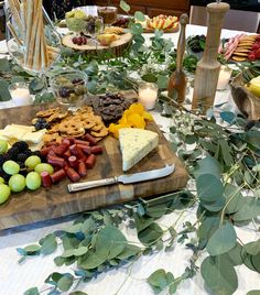 a wooden cutting board topped with grapes and cheese next to other foods on a table