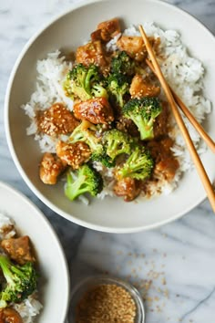 two bowls filled with rice, broccoli and chicken next to chopsticks