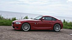 a red sports car parked on the side of a road next to the ocean and grass