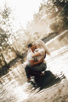 a man and woman are kissing in the middle of a body of water with trees behind them