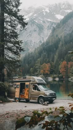 a van parked in front of a lake with mountains in the background and trees around it