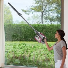 a woman standing in front of a window holding a cordless lawn mower