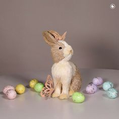 a stuffed rabbit sitting in front of some painted eggs on a table with a gray background