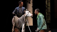 two men standing next to each other near a statue of a cow on a rope