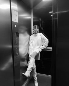 a woman in white boots is standing on the elevator door with her leg up and looking at the camera