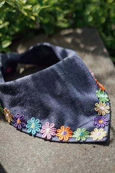 a black bandana with multicolored flowers on it sitting in front of some bushes