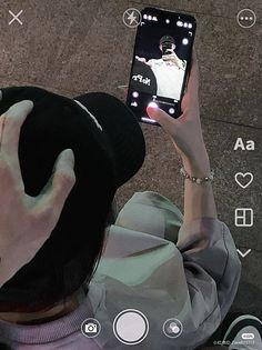 a person wearing a black hat and holding up a cell phone to take a selfie