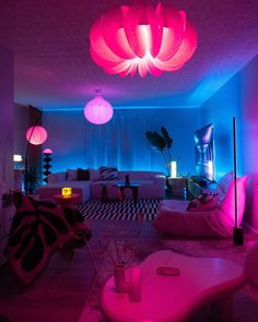 a living room filled with lots of furniture and pink lights hanging from the ceiling above