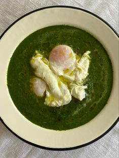 a white bowl filled with green soup topped with two poached eggs on top