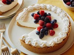 a cheesecake topped with berries and blueberries on top of a white plate next to silverware