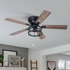 a black ceiling fan with wooden blades in a living room next to a white fireplace