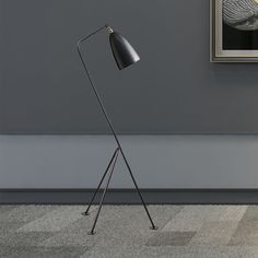 a black floor lamp sitting on top of a wooden table next to a painting and a framed picture