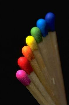 five colored pencils lined up in a row on a black background, with the colors of the rainbow visible