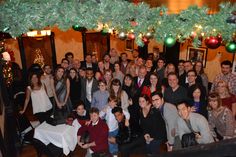 a large group of people posing for a photo in front of christmas decorations and lights