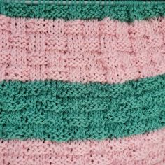 a pink and green crocheted bag with stripes on it's side, sitting on a table