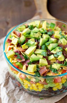 a glass bowl filled with corn and avocado on top of a wooden table