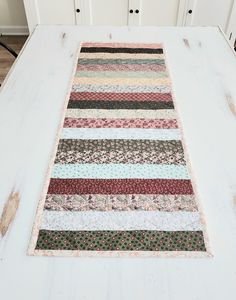 a white table topped with a rug covered in multicolored strips and flowers on top of it