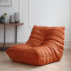 an orange bean bag chair sitting on top of a hard wood floor next to a table