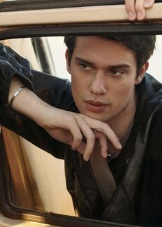 a young man looking out the window of a car with his hand on his tie