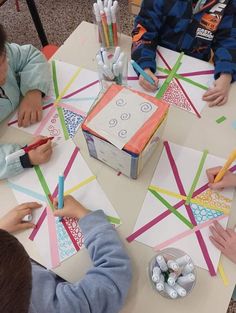 children are sitting at a table making crafts with crayons and colored pencils