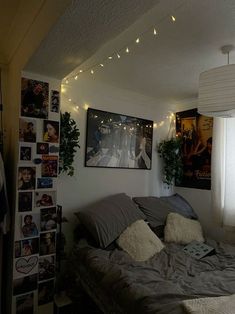 an unmade bed in a small room with pictures on the wall and lights strung from the ceiling