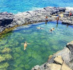 people are swimming in the water near some rocks