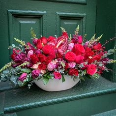 a white bowl filled with red and pink flowers sitting on top of a green door