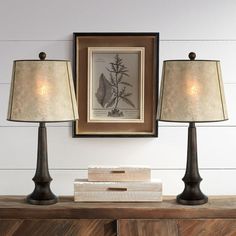 three lamps sitting on top of a wooden dresser next to a framed print and two books