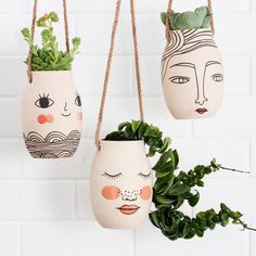 three planters with faces painted on them hanging from ropes next to a white brick wall