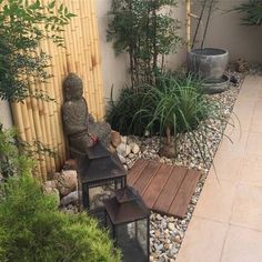 a small garden with rocks, plants and a lantern on the ground in front of a bamboo fence