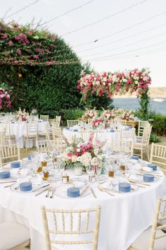 a table set up with white linens and blue place settings for an outdoor wedding