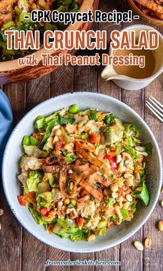 thai crunch salad with peanut dressing in a white bowl on a wooden table next to other dishes and utensils