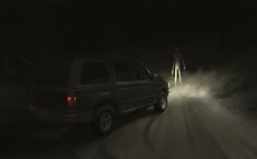 two people standing on the side of a road at night with fog coming from behind them