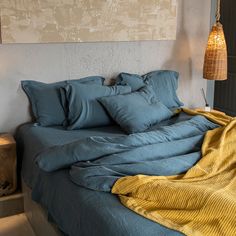 an unmade bed with blue sheets and yellow blankets on it, next to a lamp