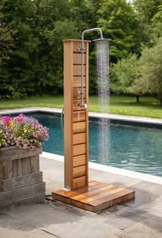 an outdoor shower in front of a swimming pool with flowers and potted plants next to it