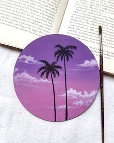 a painting of two palm trees in front of an open book with a paintbrush