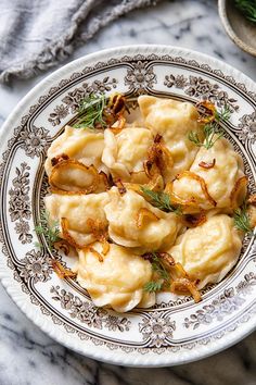 a white plate topped with dumplings on top of a marble table next to silverware