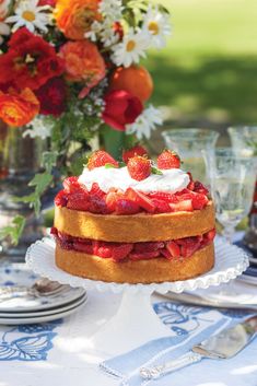 a cake sitting on top of a table covered in frosting and strawberries next to a vase filled with flowers