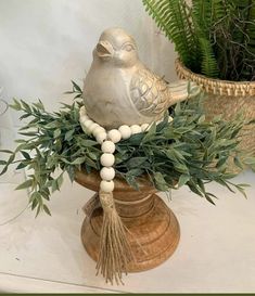 a bird statue sitting on top of a vase filled with green leaves and beads next to a potted plant