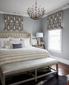 a bedroom with a bed, chandelier and window coverings in shades of gray