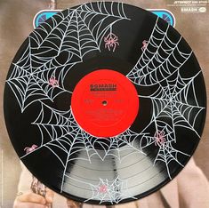 a black and red record with spider webs on the side, in front of a woman's hand