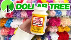 a hand holding a bottle of mod podge paint in front of colorful crocheted flowers