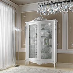 a white china cabinet with glass doors and chandelier