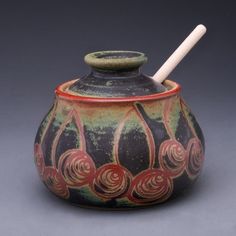 a ceramic jar with a white handle and red flowers painted on the outside, sitting on a gray surface