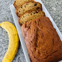 a loaf of banana bread sitting on top of a white plate next to a ripe banana