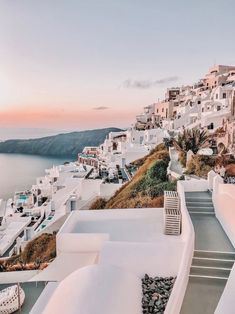 the sun is setting over some white buildings on the cliff overlooking the water and mountains