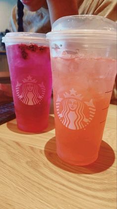 two drinks sitting next to each other on top of a wooden table in front of a woman